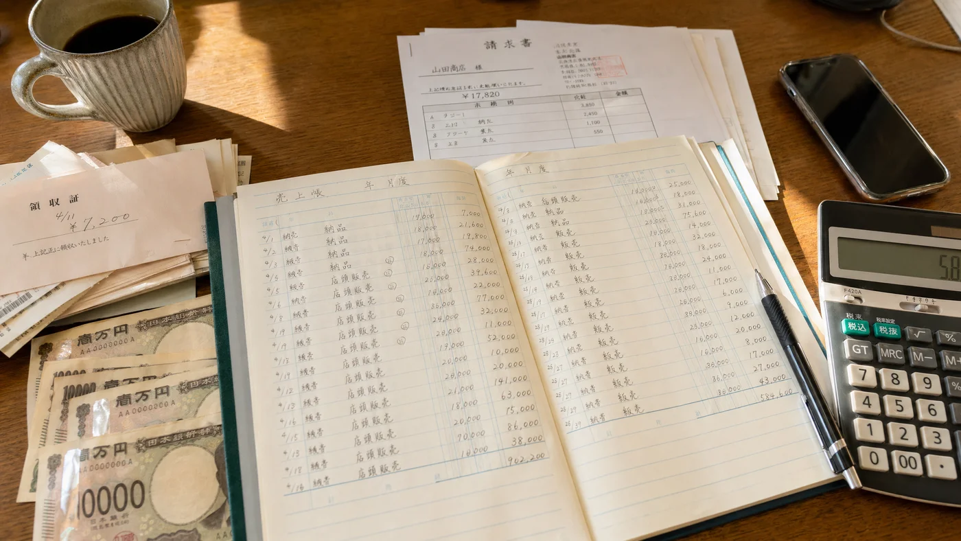 個人事業主のデスクで売掛金台帳と支払い予定表が並ぶ資金繰りのイメージ